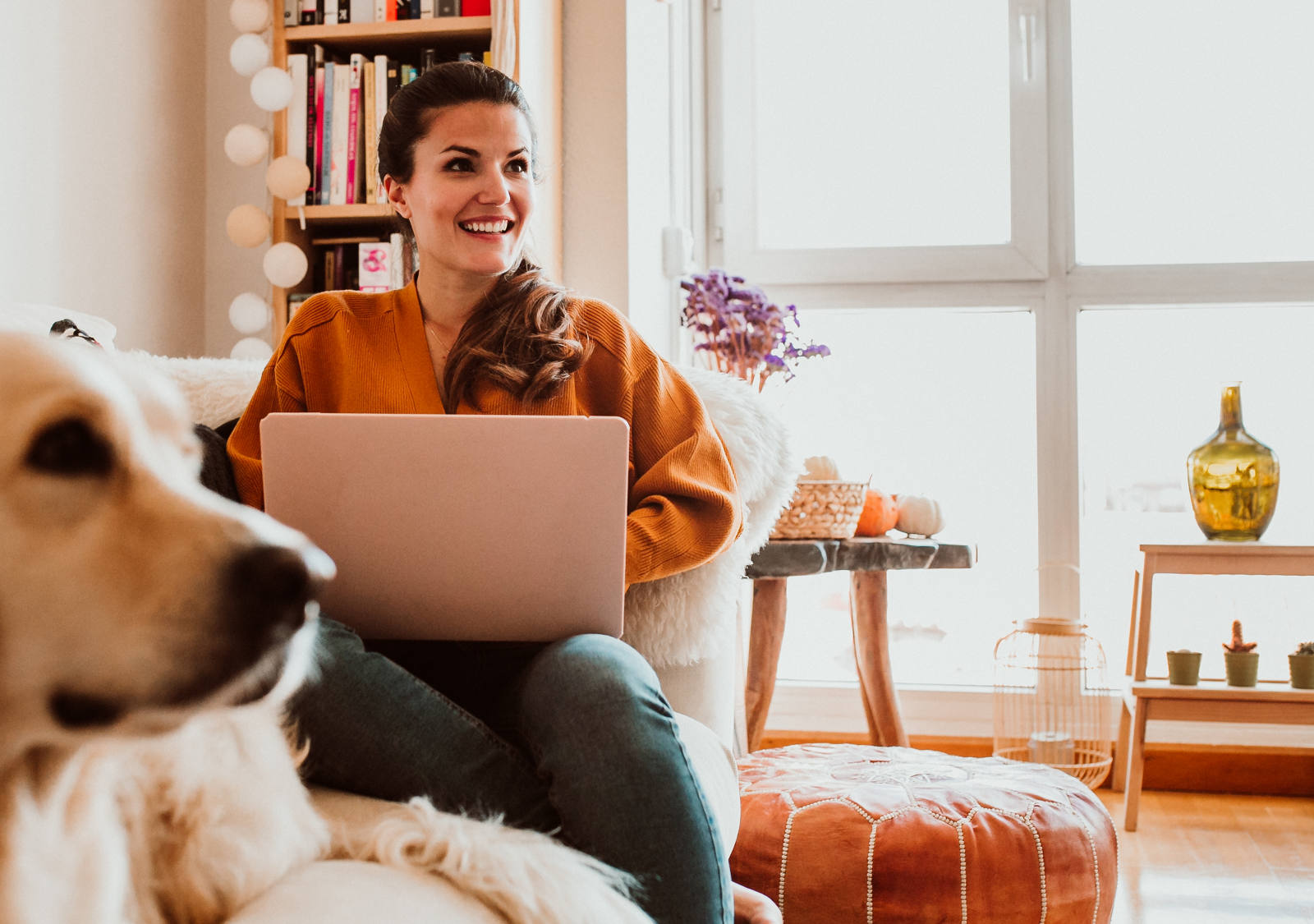 Frau sitzt neben Ihrem Hund auf dem Sofa und arbeitet am Laptop