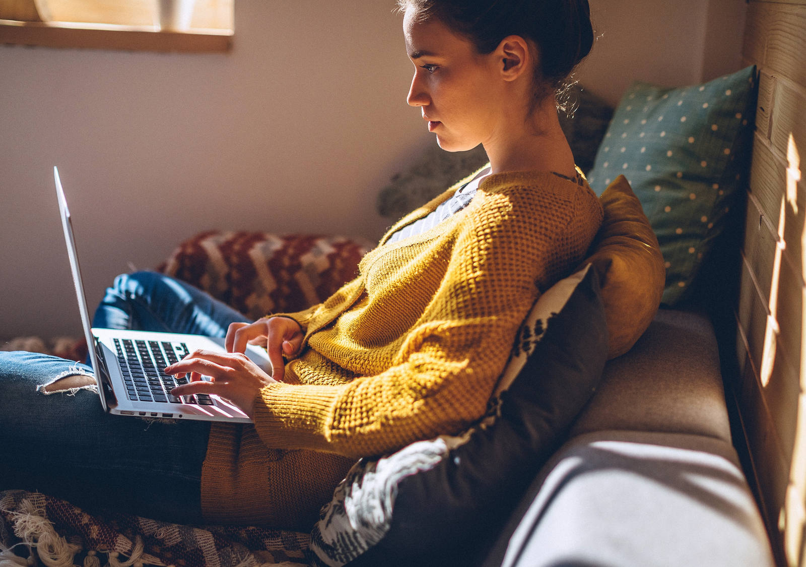 Donna si siede con il computer portatile sulle gambe sul divano