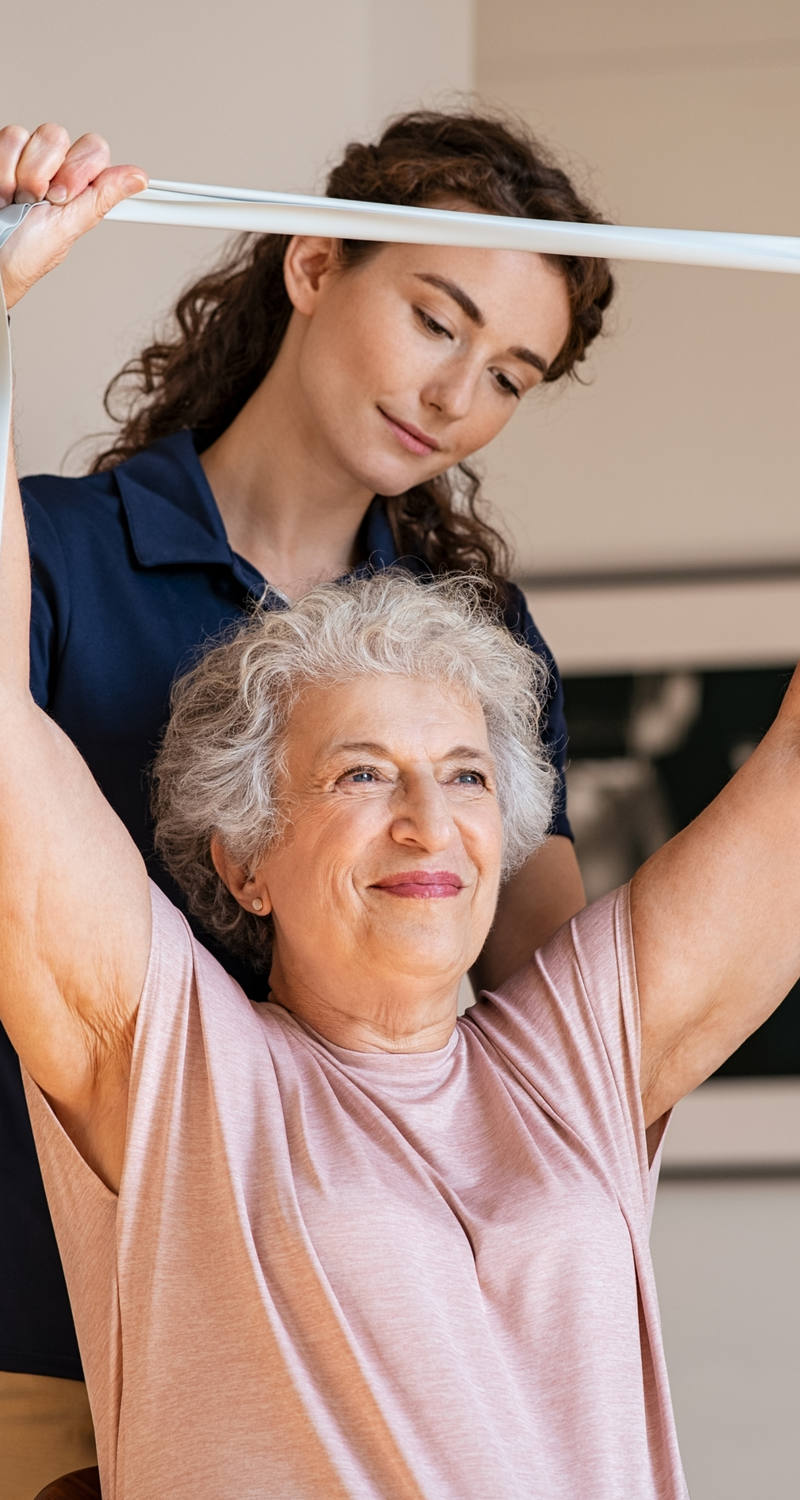  An older woman exercises with a stretch band, led by another woman