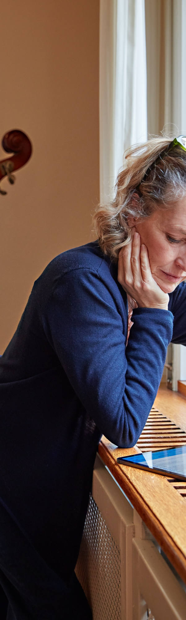 Frau studiert Tablet vor ihrem Cello am Fenster