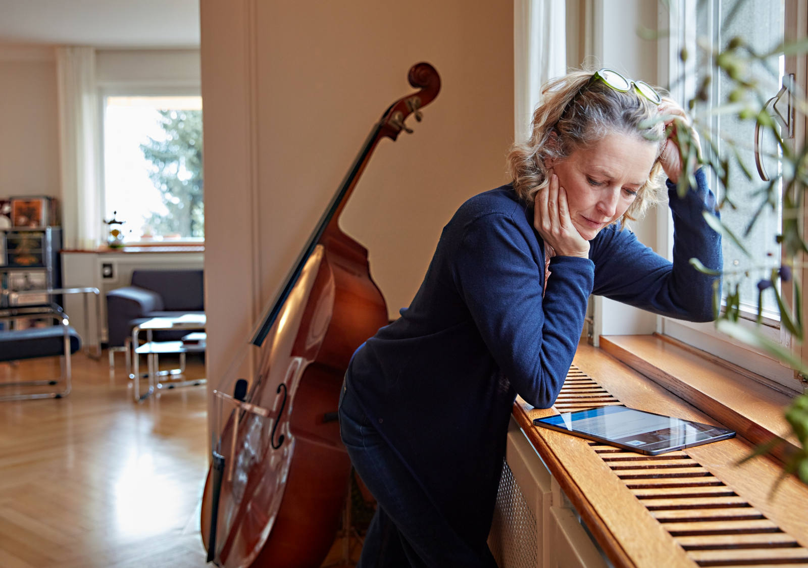 Frau studiert Tablet vor ihrem Cello am Fenster