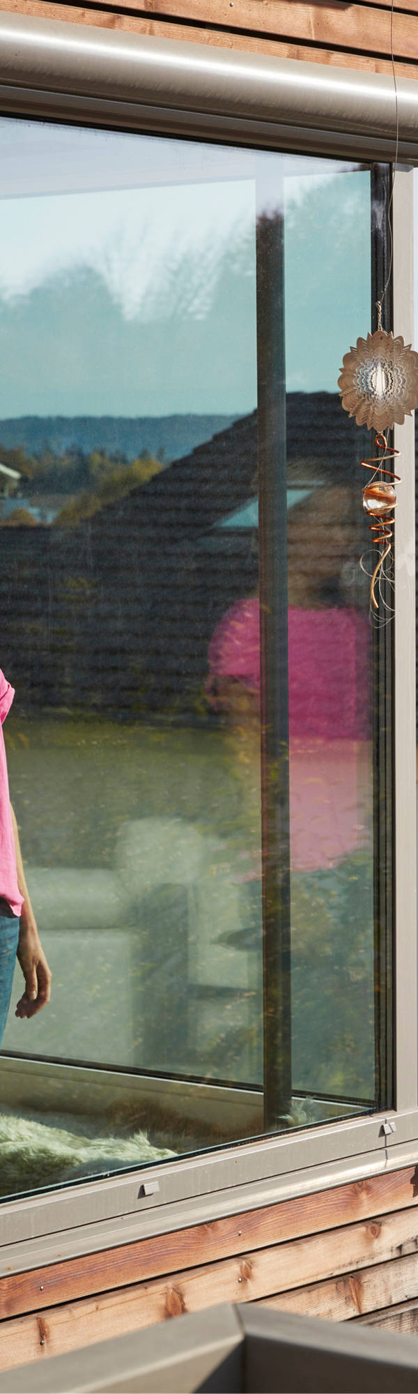  A woman is standing at a large window making a phone call.