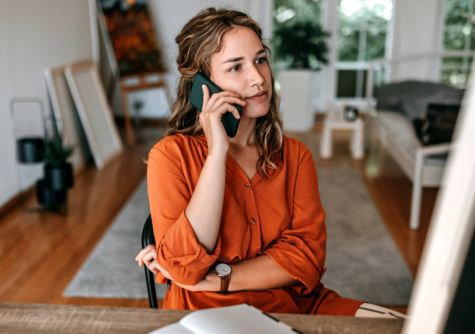 Woman is sitting at the table making an attentive phone call. In front of her is an open notebook.