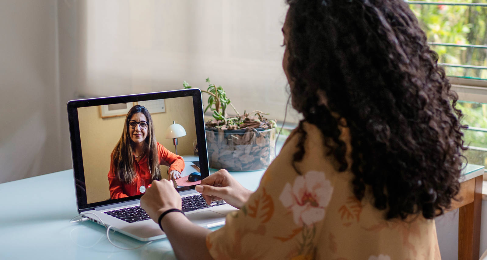 Woman sits at the table with her laptop and has a digital therapy session.