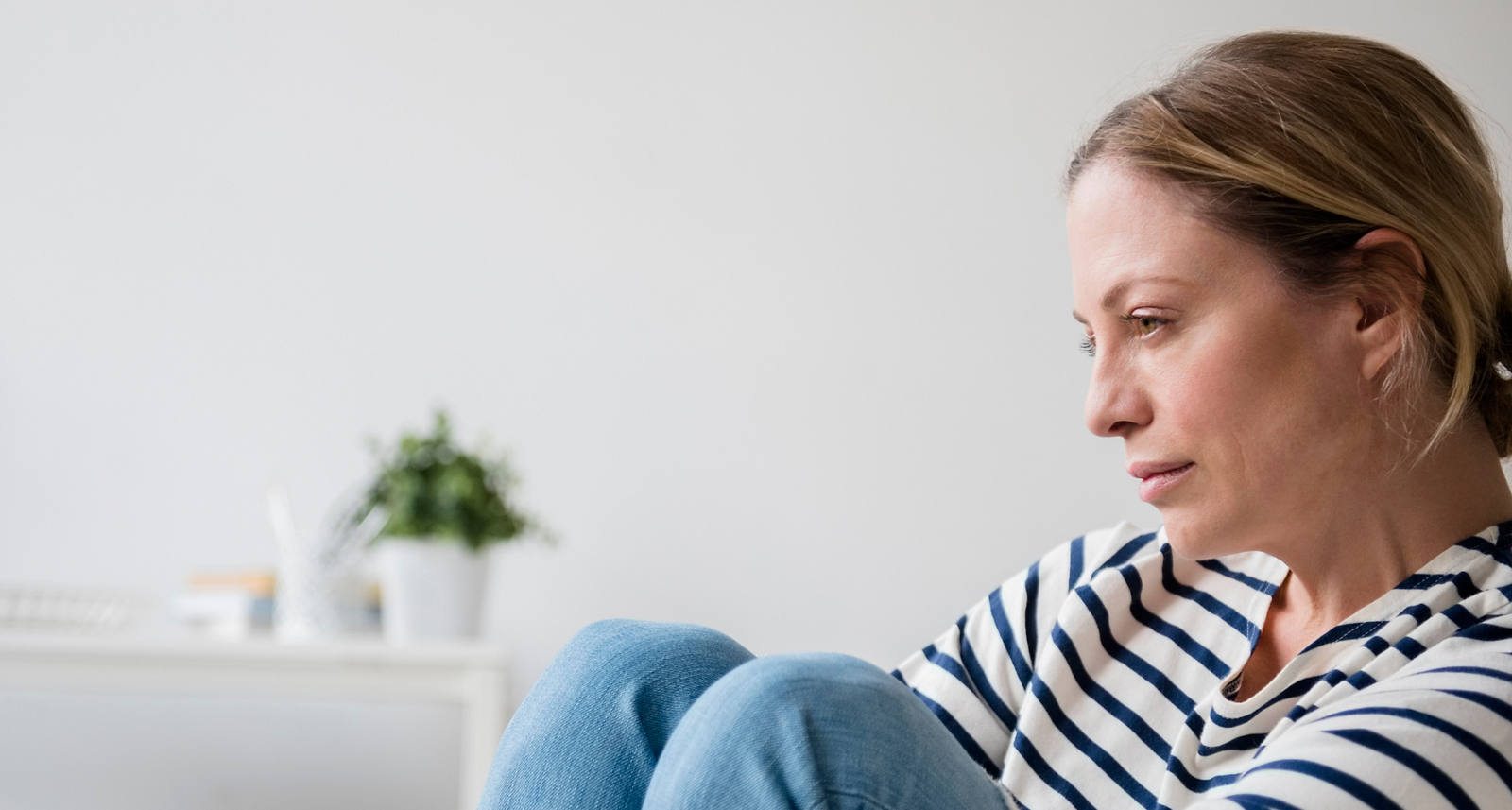 Traurige Frau sitzt mit angezogenen Beinen auf einem Sessel.