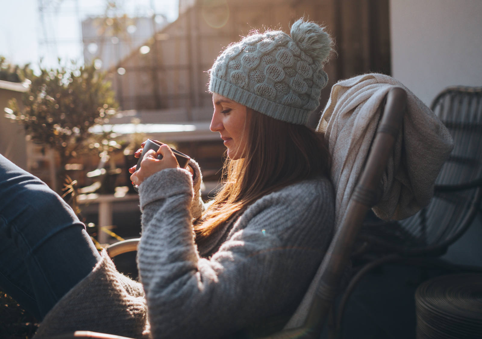 Frau sitz auf dem Balkon in Stuhl und geniesst erste Sonnenstrahlen im Frühling.