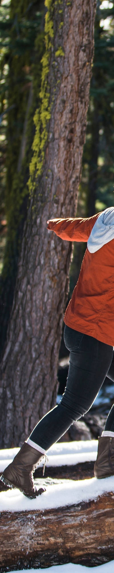 Una donna è in equilibrio nel bosco su un tronco innevato.