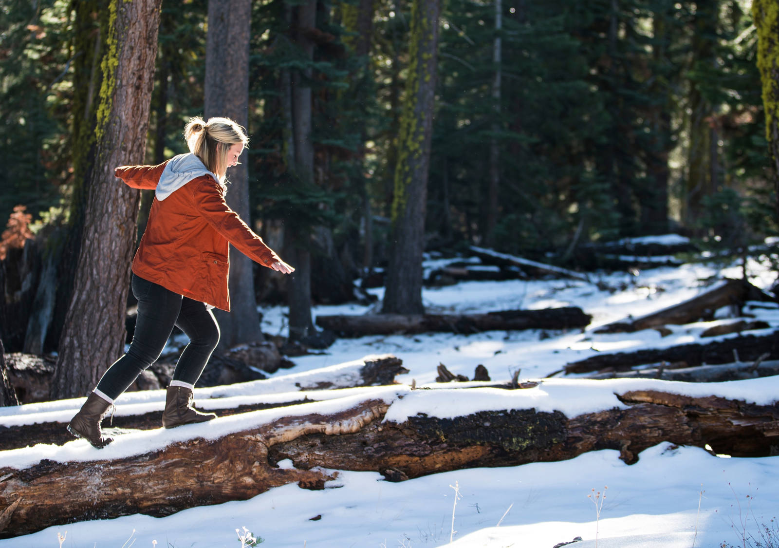 A woman balances in the forest on a snow-covered tree trunk.