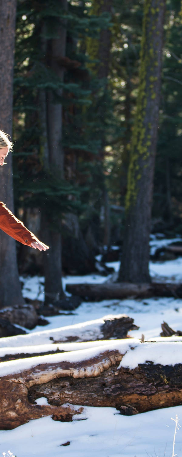 Une femme se tient en équilibre dans la forêt sur un tronc d’arbre couvert de neige.