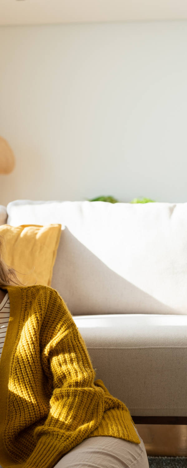 Eine müde Frau sitzt vor dem Sofa auf dem Boden und fasst sich erschöpft an die Stirn.