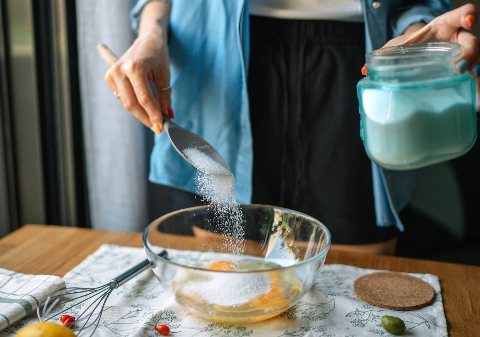 Frau backt in Küche und streut Industrie-Zucker in eine Schüssel mit zerschlagenen Eiern.