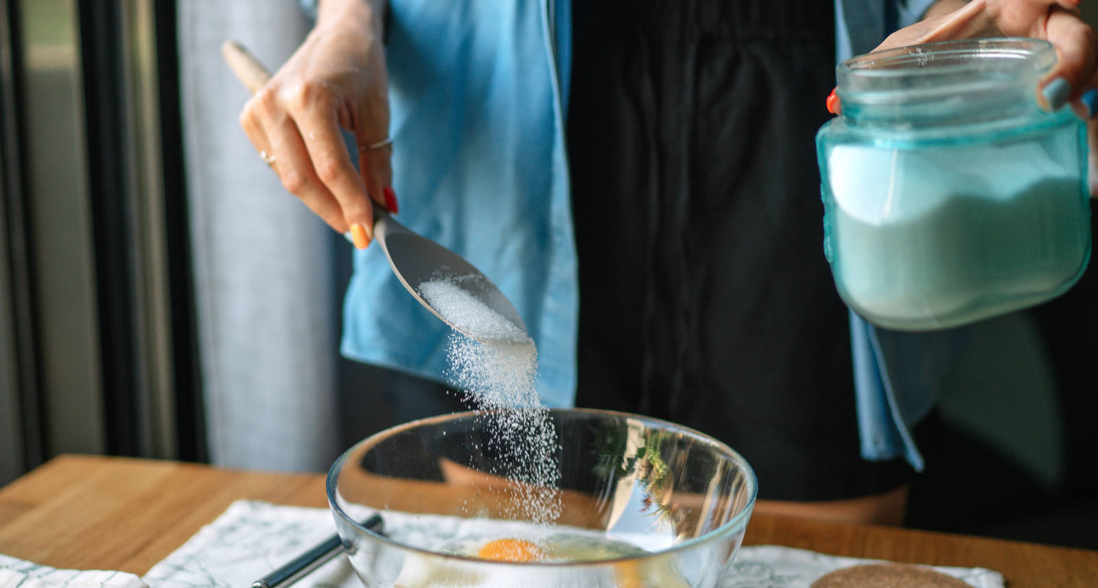 Frau backt in Küche und streut Industrie-Zucker in eine Schüssel mit zerschlagenen Eiern.