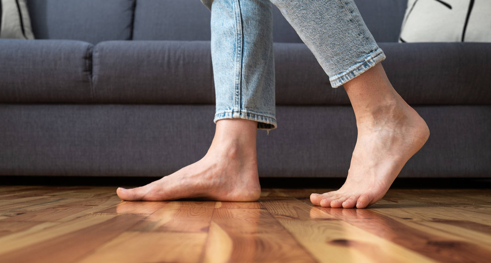 Une femme marche pieds nus dans le salon sur du parquet.