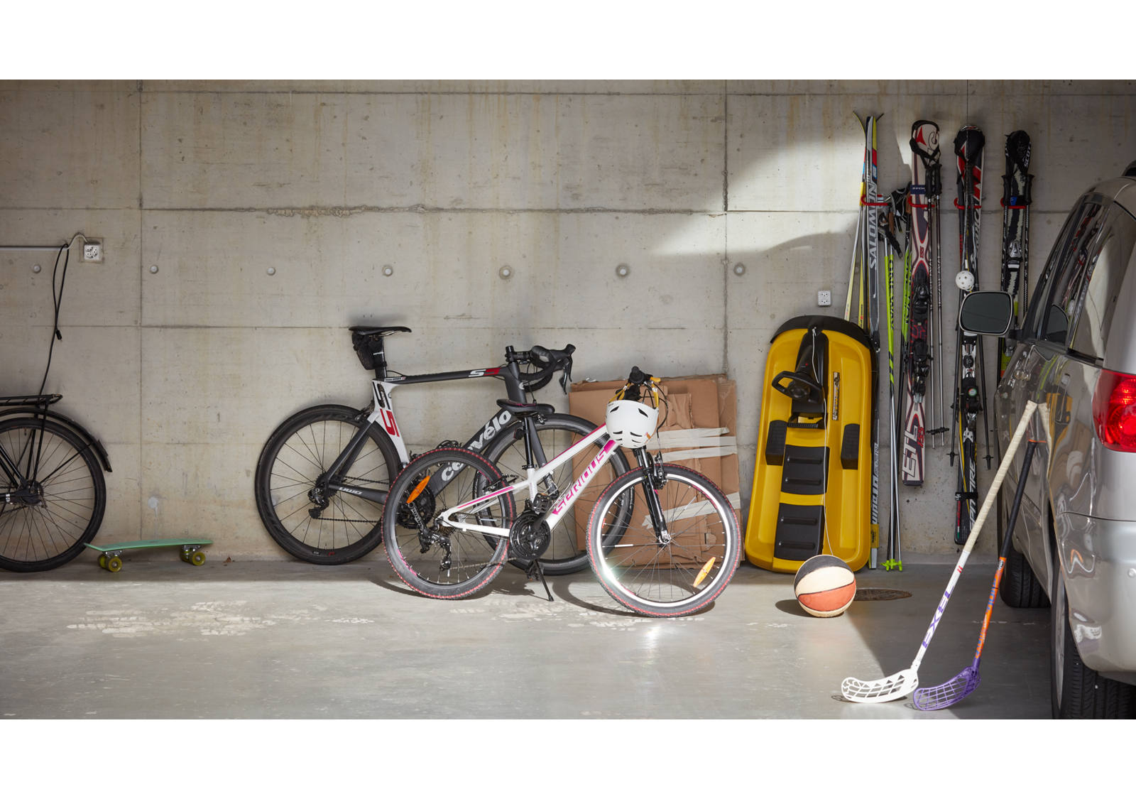 Fahrräder stehen neben dem Auto und anderen Sport-Utensilien in der Garage.