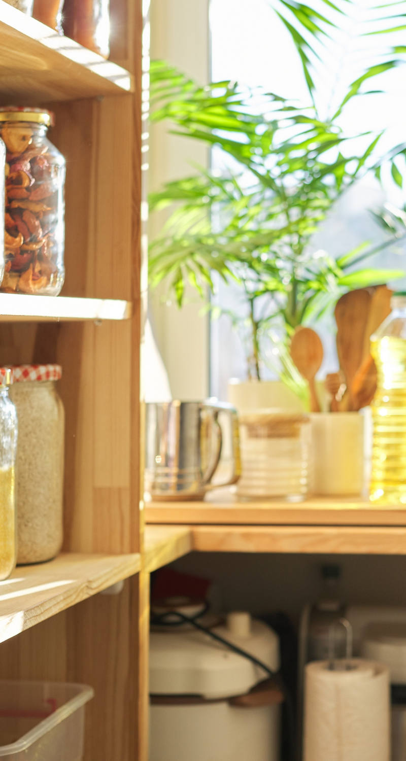 On a kitchen shelf there are lots of assorted preserving jars. They are filled with all sorts of things.