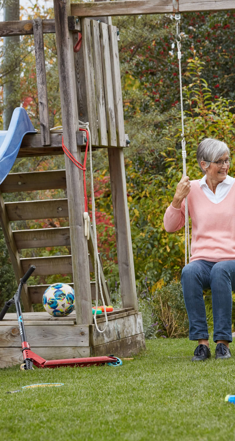 Junge spielt Fussball im Garten und Grossmutter schaukelt im Hintergrund