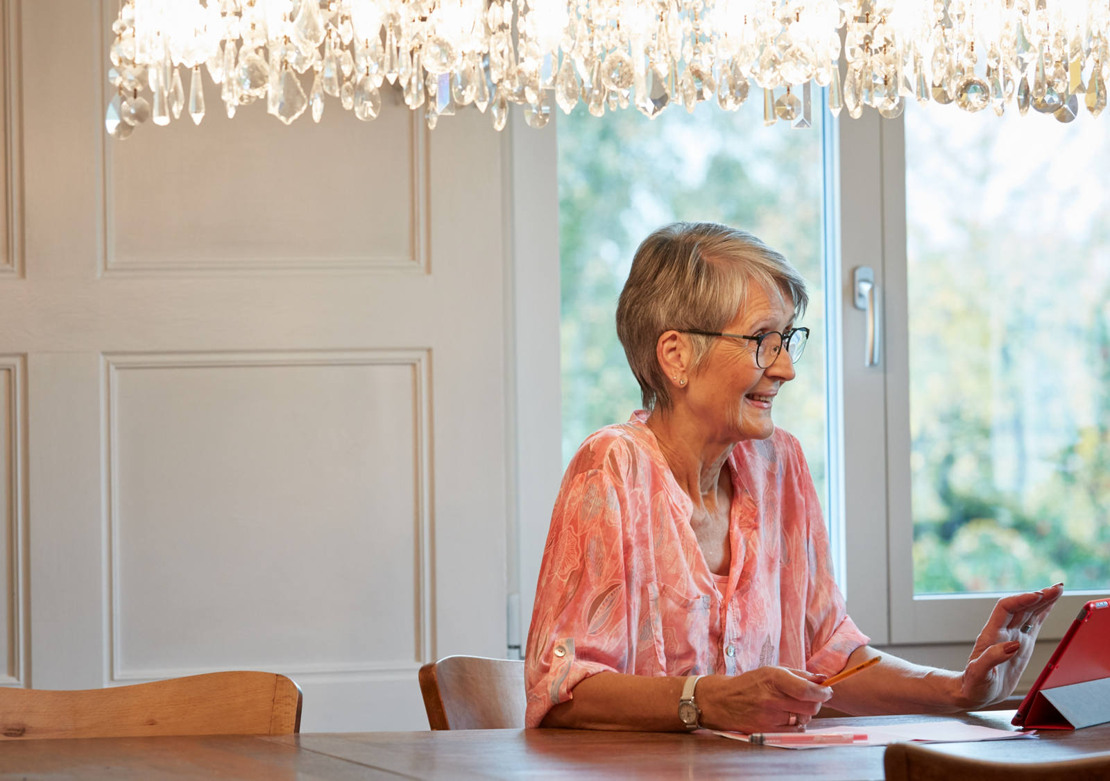 Grossmutter sitzt am Tisch und ist am Tablet.