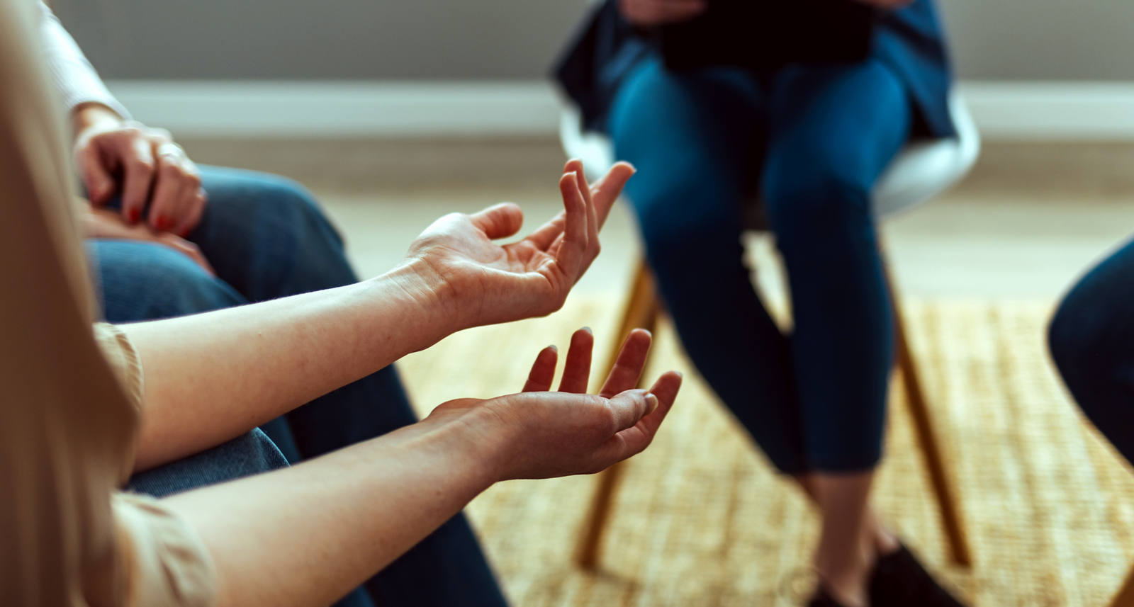 Eine Gruppe Menschen sitzt im Kreis, der Fokus ist auf die Hände der Frau gerichtet.
