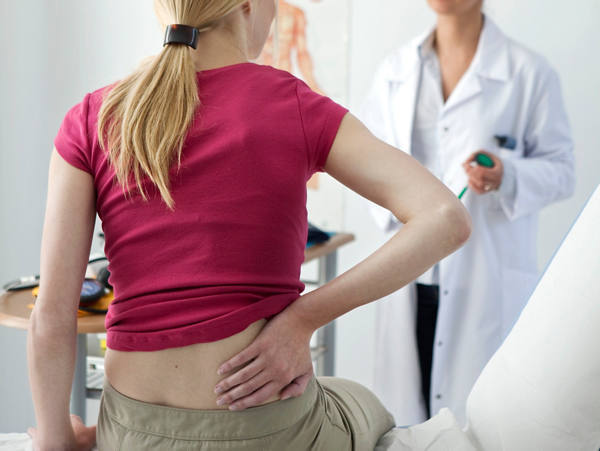 Frau ist bei Ärztin in einer Sprechstunde und hat Schmerzen im Rückenbereich.
