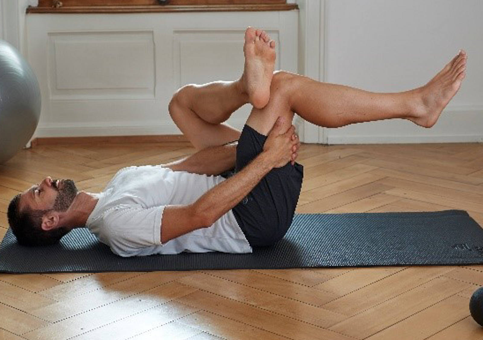 Man stretches the buttock muscles by bending the right leg while lying on his back