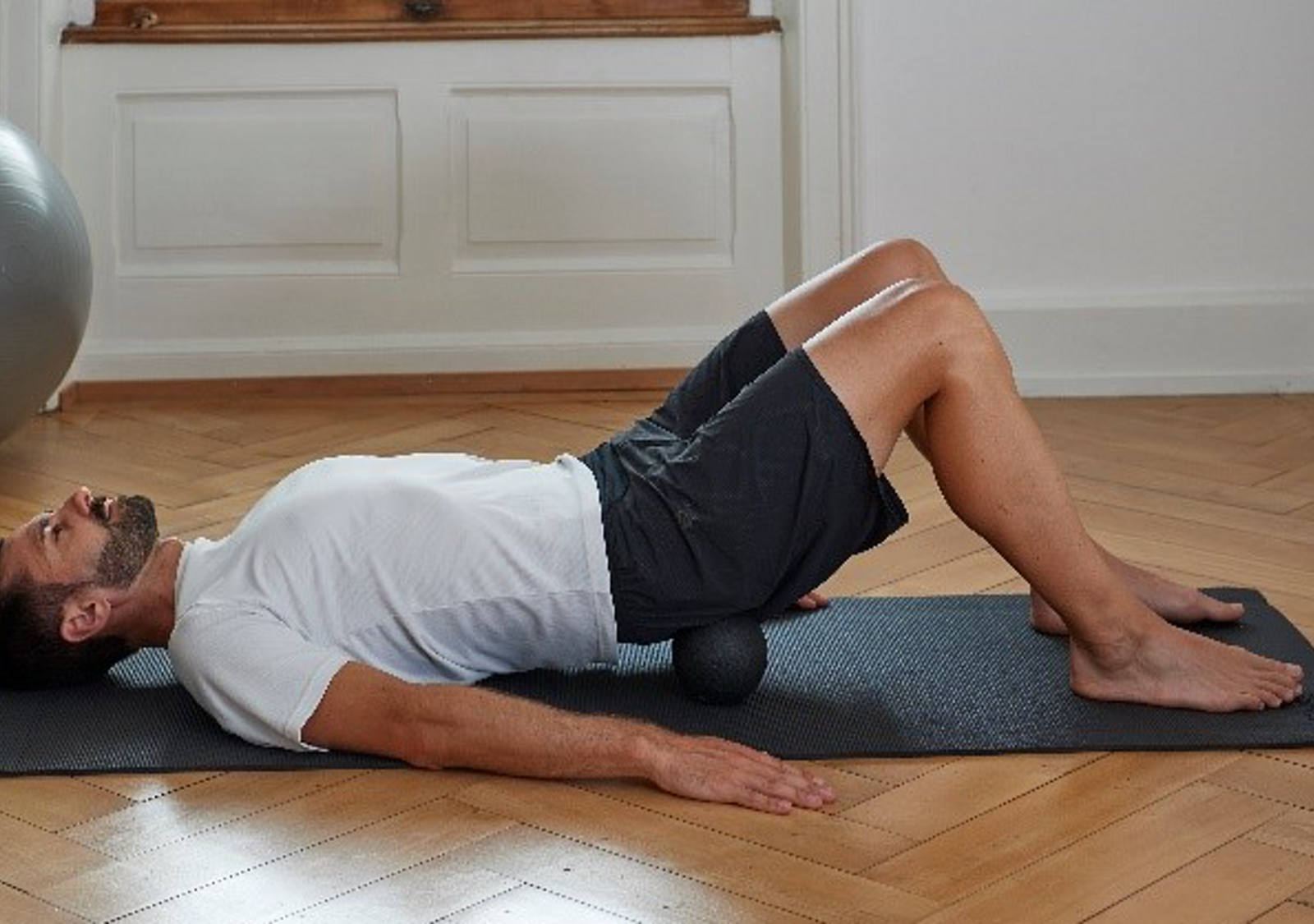 Man lies on his back and massages tense buttock muscles with a fascia ball