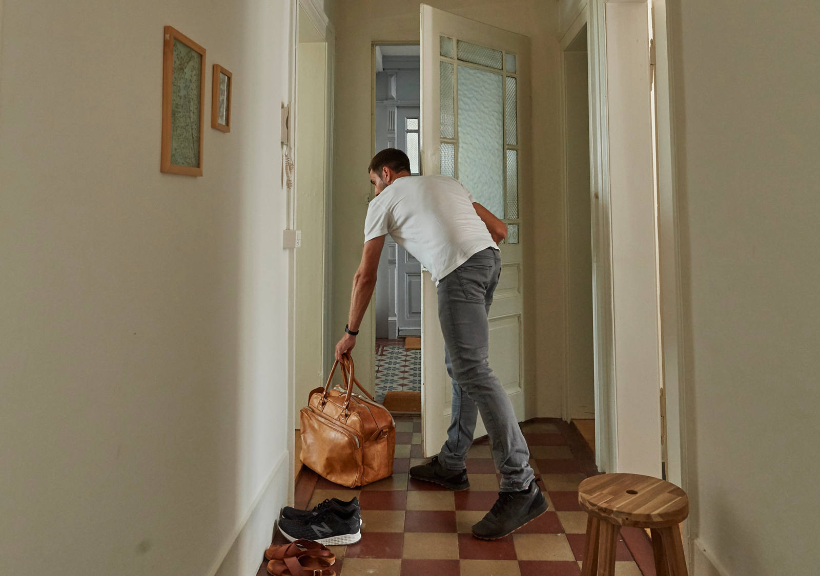 Un homme se tient dans le couloir, ouvre la porte et saisit son sac de voyage.