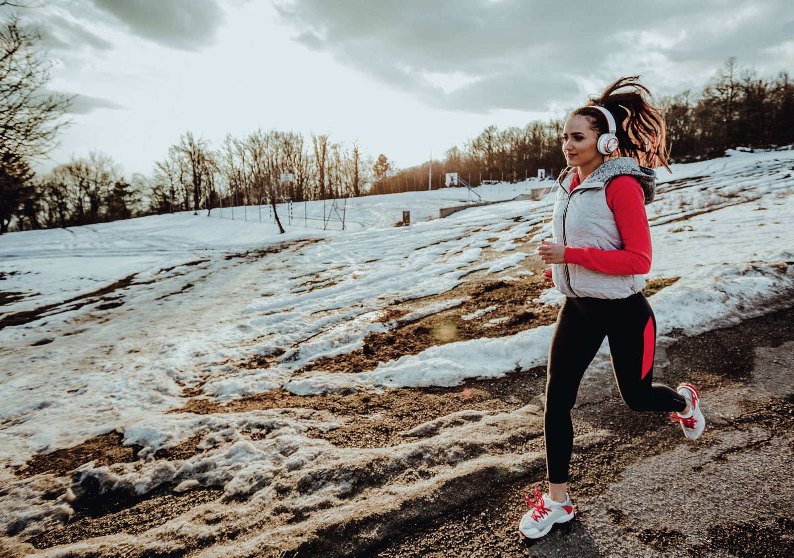 Woman with headphones jogging through a winter landscape