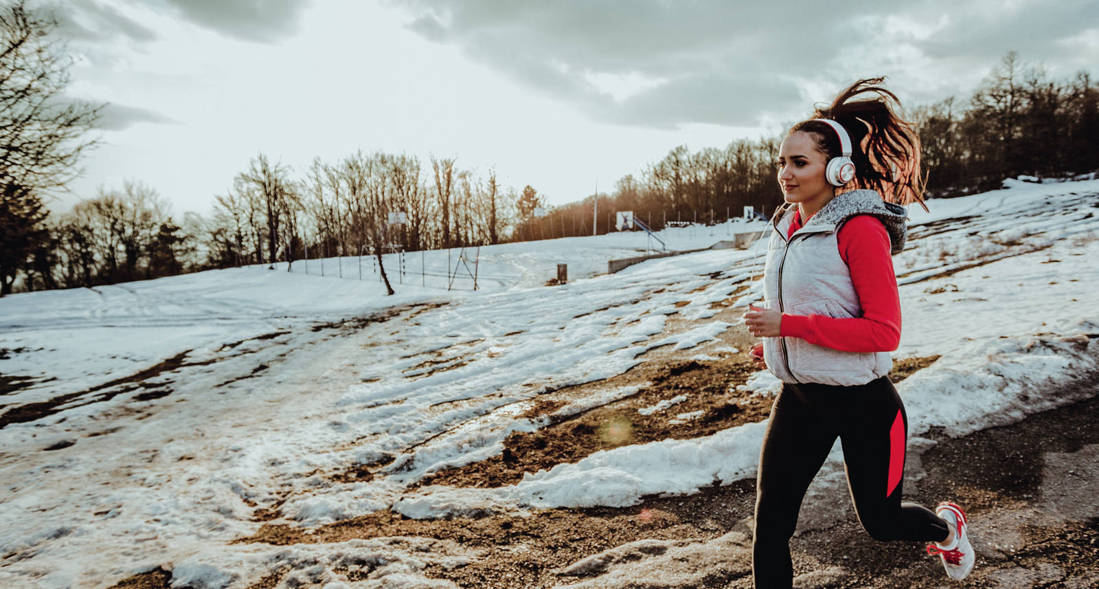 Woman with headphones jogging through a winter landscape