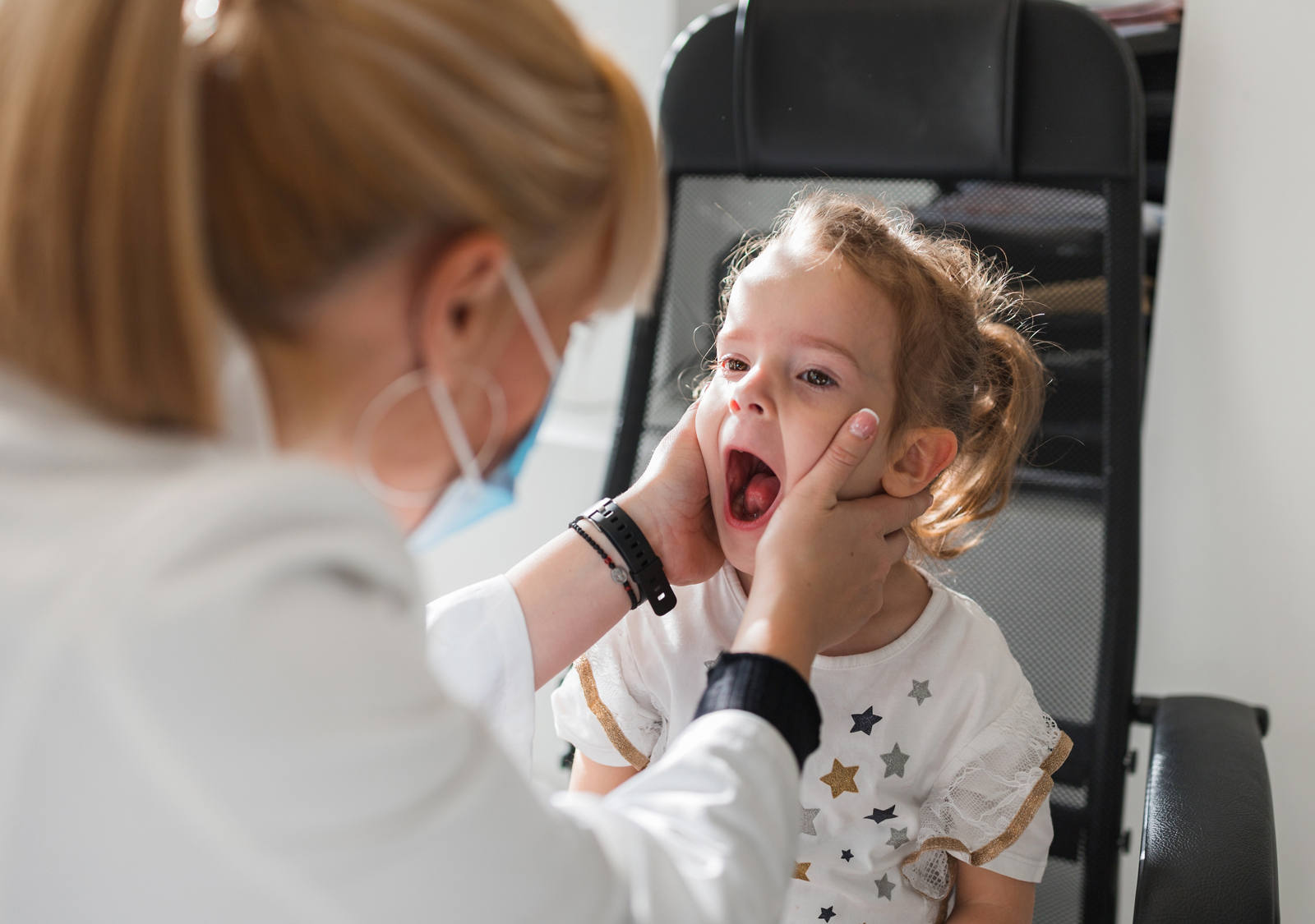 Kleines Kind, dessen Mandeln und Rachen von einer Ärztin untersucht werden.