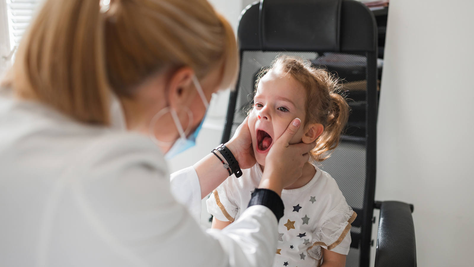 Kleines Kind, dessen Mandeln und Rachen von einer Ärztin untersucht werden.