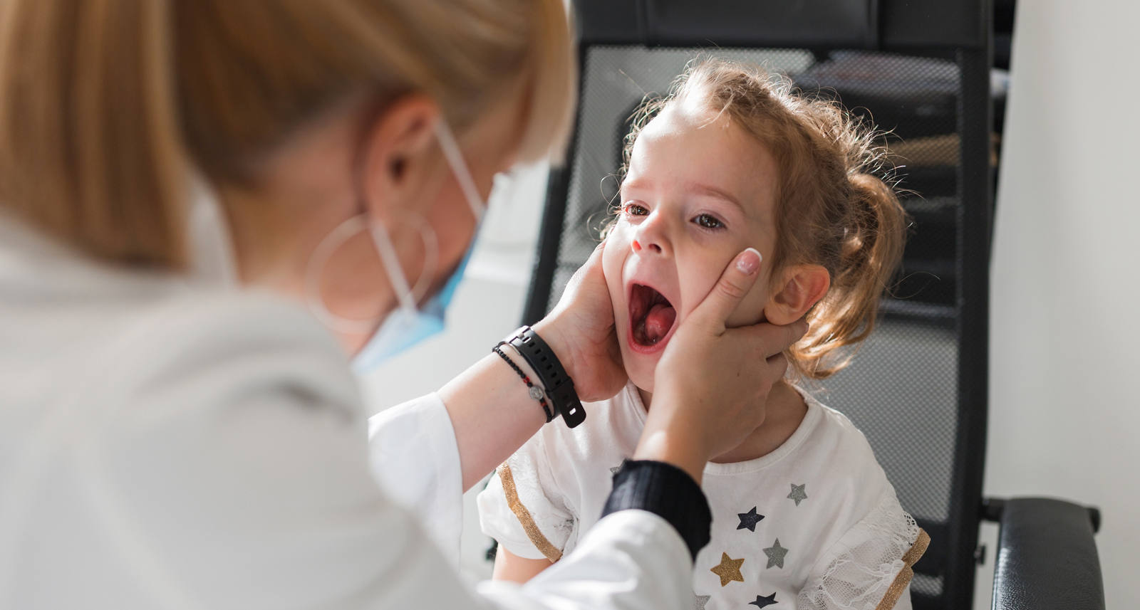 Kleines Kind, dessen Mandeln und Rachen von einer Ärztin untersucht werden.
