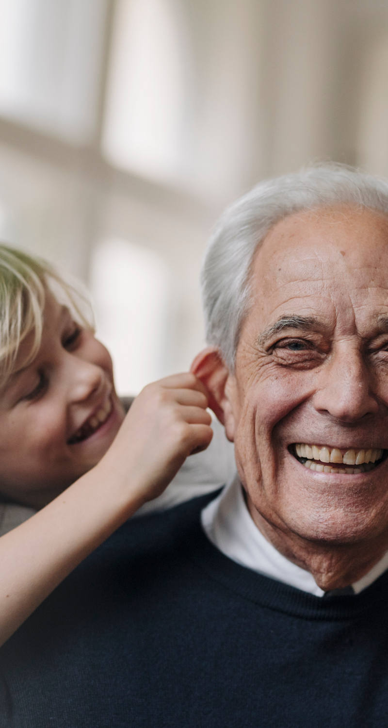 A little boy pulls an old man’s ears long, and both laugh warmly