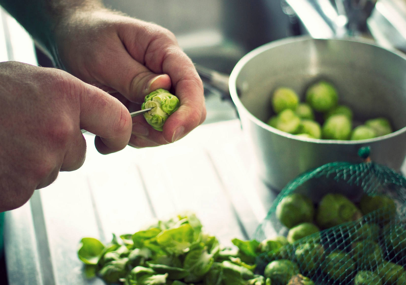 Un homme a lavé tout un filet de choux de Bruxelles dans la cuisine et les prépare maintenant avec un couteau.