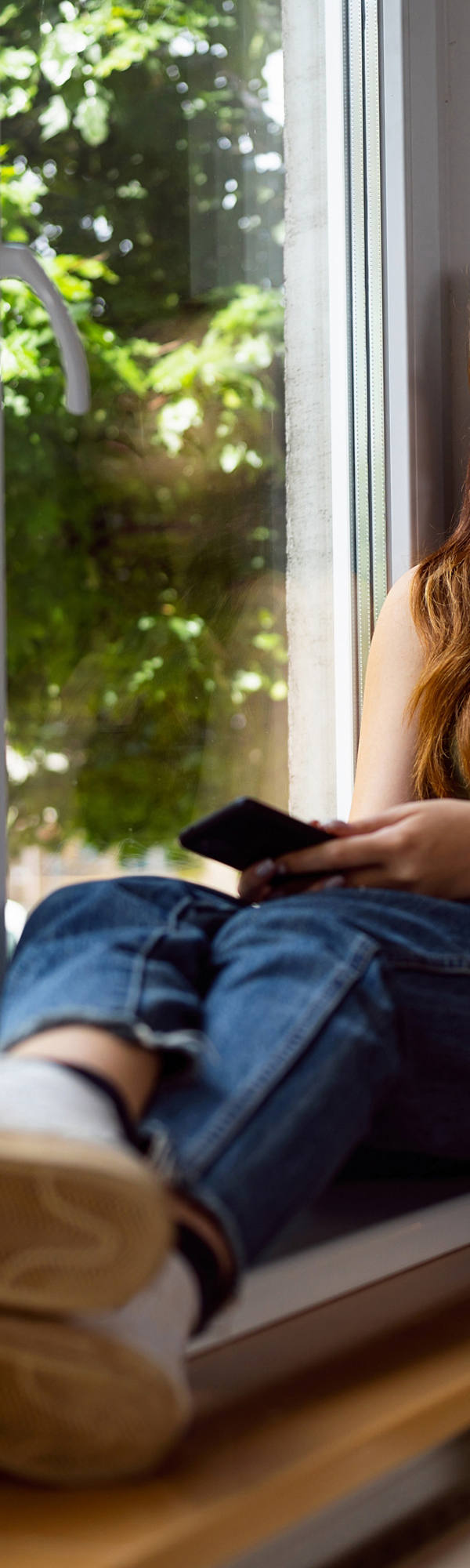 Eine junge Frau sitzt am Fenster und schaut traurig