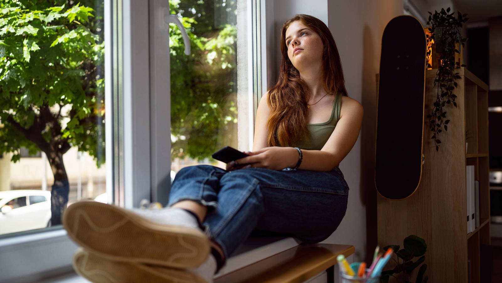 Eine junge Frau sitzt am Fenster und schaut traurig
