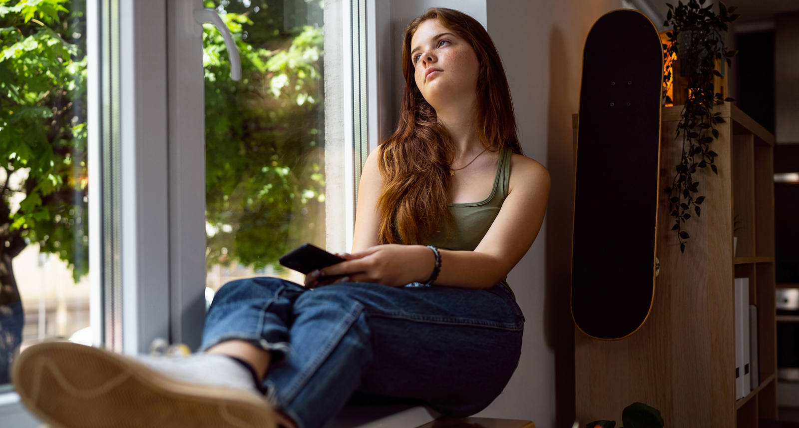 Eine junge Frau sitzt am Fenster und schaut traurig