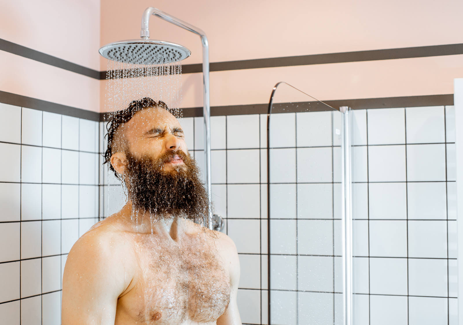 A middle-aged man with a beard stands in the shower with cold water running over him.