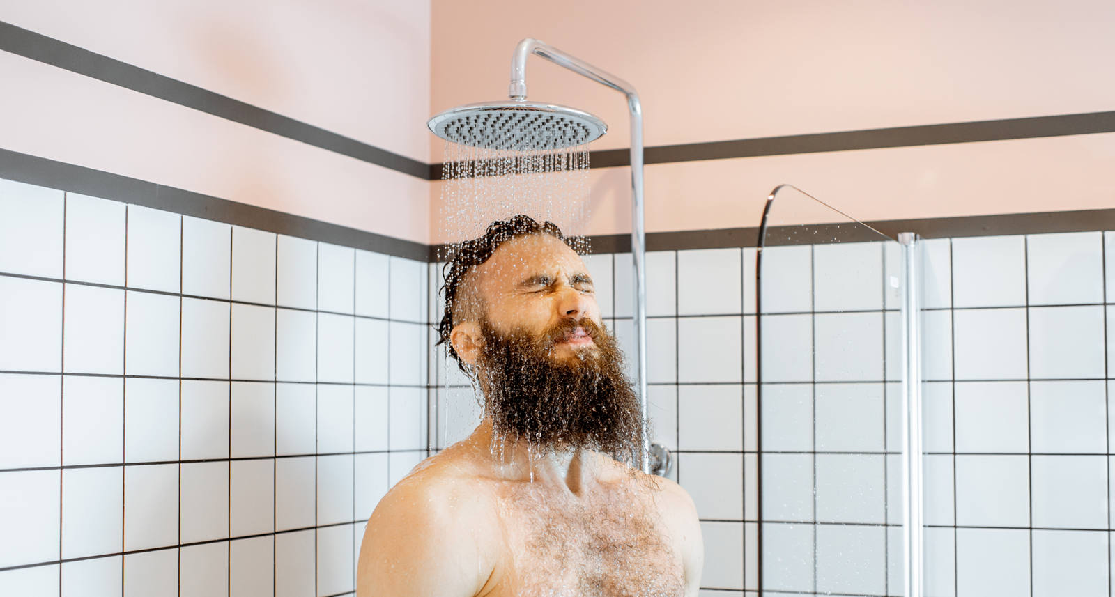 A middle-aged man with a beard stands in the shower with cold water running over him.