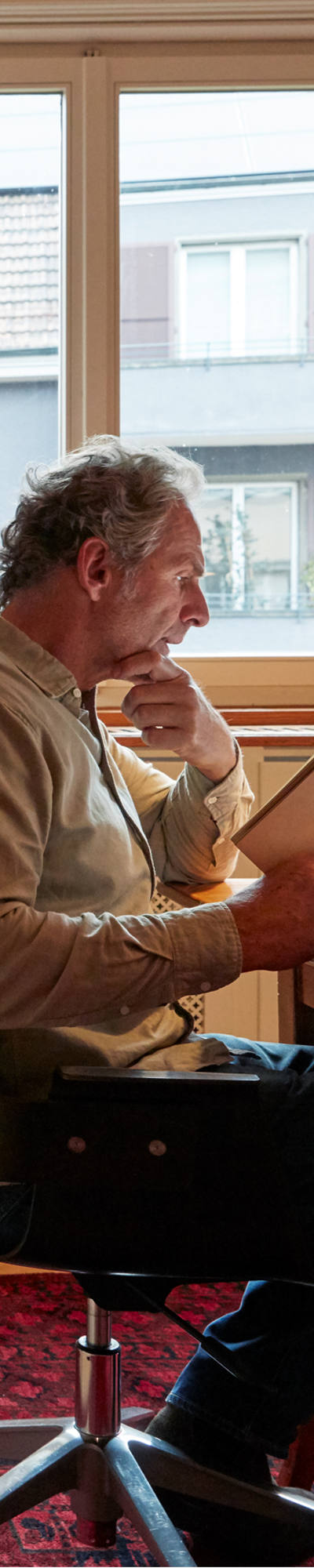 Man studying book in his home office. In the background is a huge book wall.