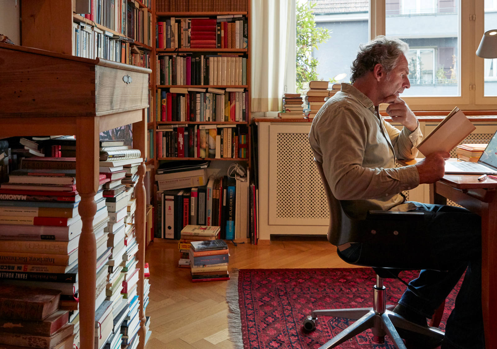 Uomo studia libro nel suo ufficio a casa. Sullo sfondo c’è un’enorme libreria.