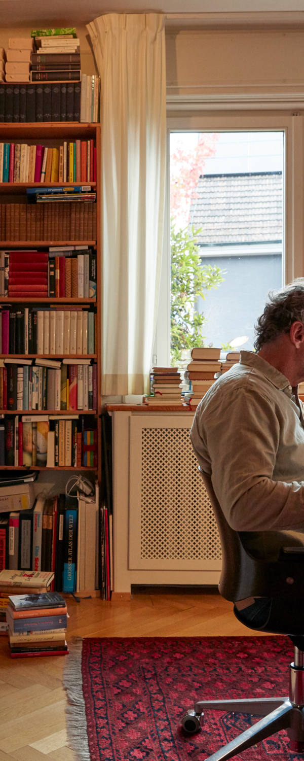 Man studying book in his home office. In the background is a huge book wall.