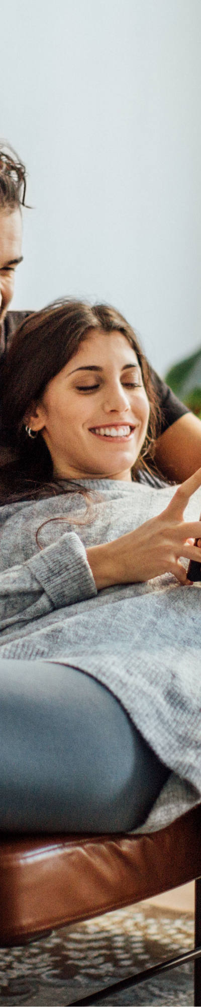 Una coppia giovane si siede sul divano e guarda felicemente smartphone.