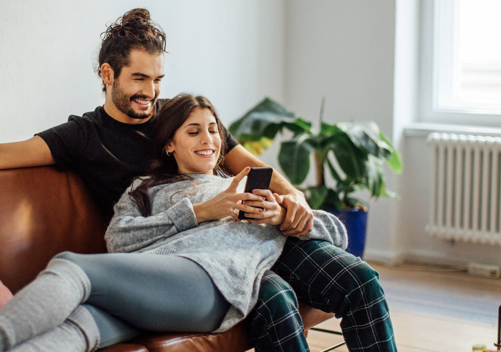 A young couple is sitting on the sofa and looking happily in their smartphone.