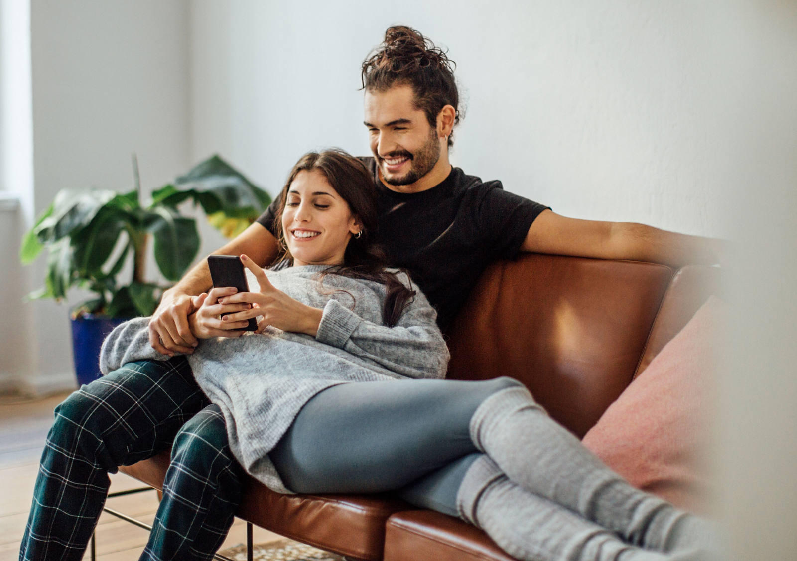 Una coppia giovane si siede sul divano e guarda felicemente smartphone.