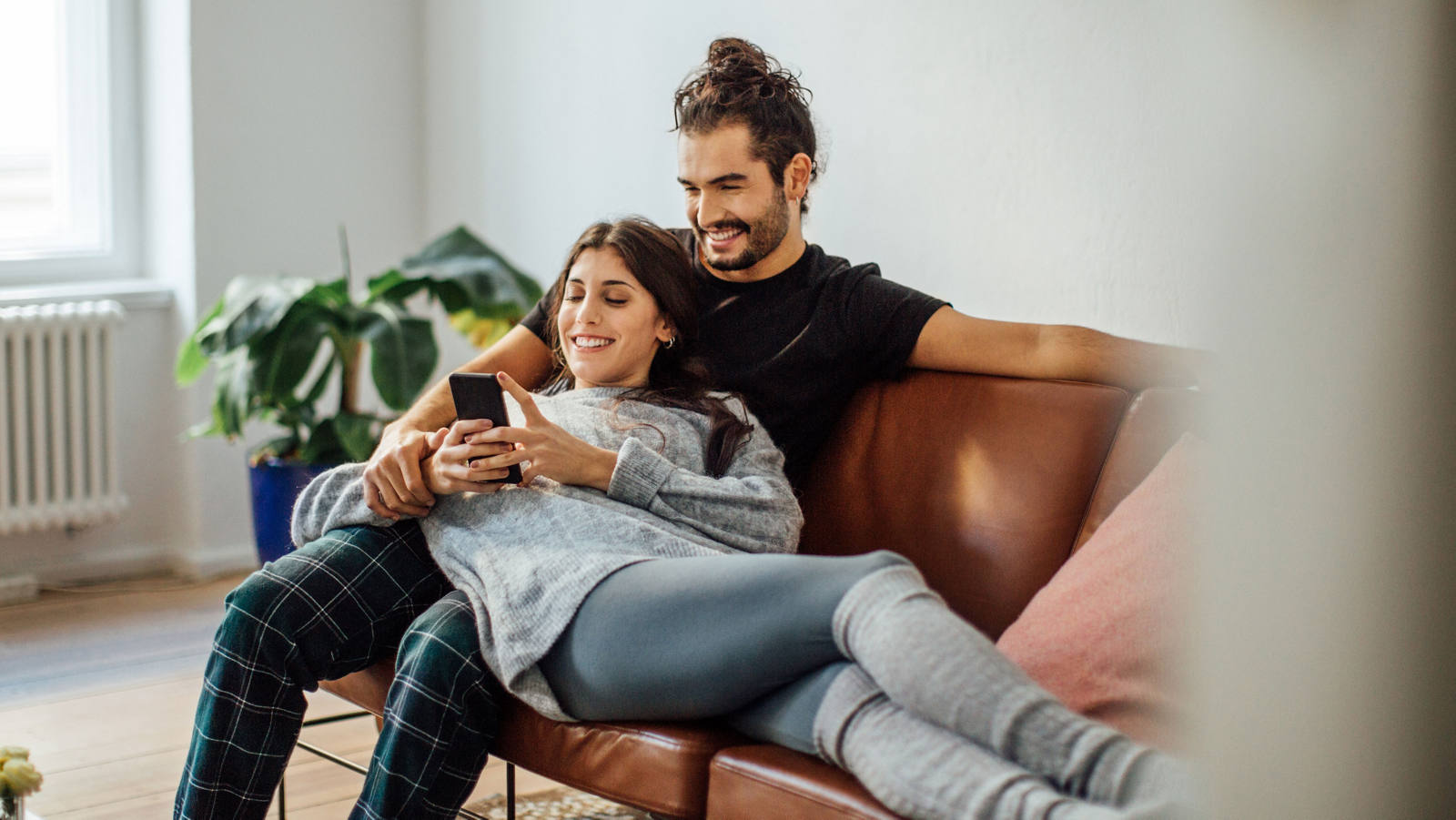 Una coppia giovane si siede sul divano e guarda felicemente smartphone.