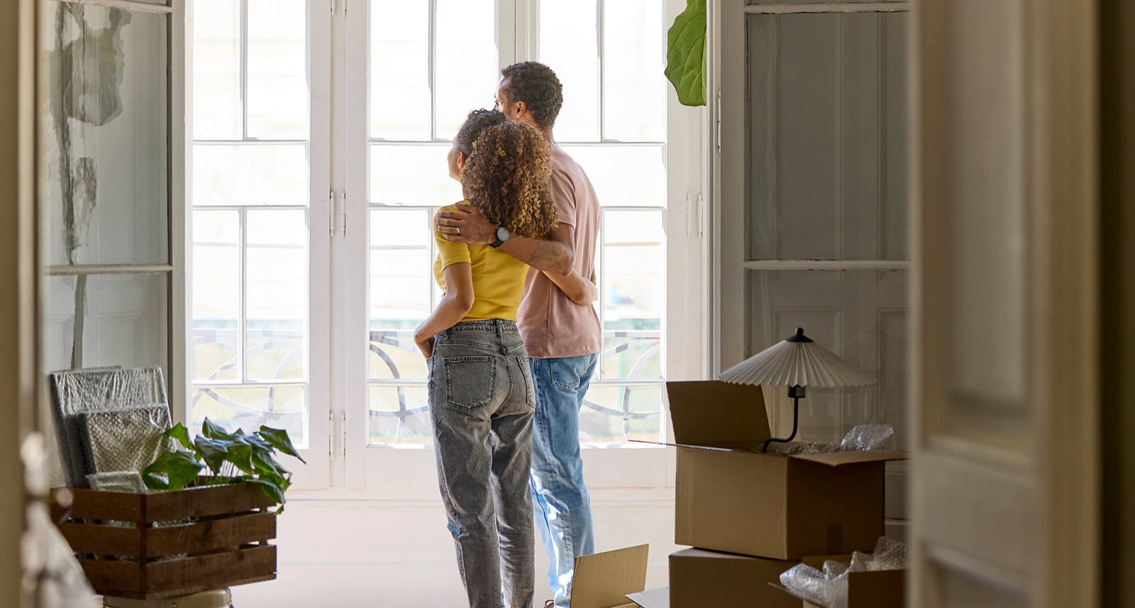  Junges Paar steht Arm in Arm in einer hellen Wohnung.