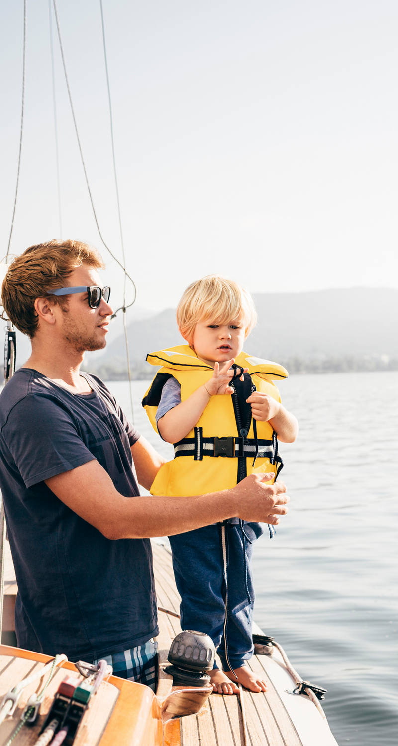 La famiglia ama una gita in barca a vela e il bambino indossa con stupore il giubbotto di salvataggio giallo