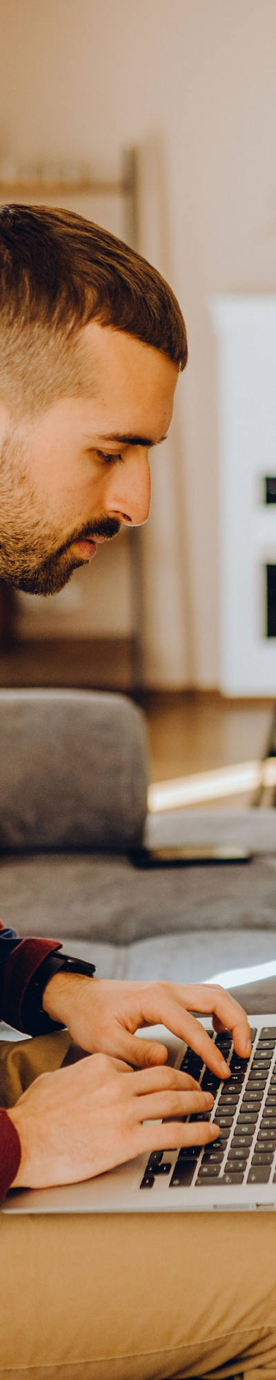 L’uomo lavora al portatile e si siede sul divano.