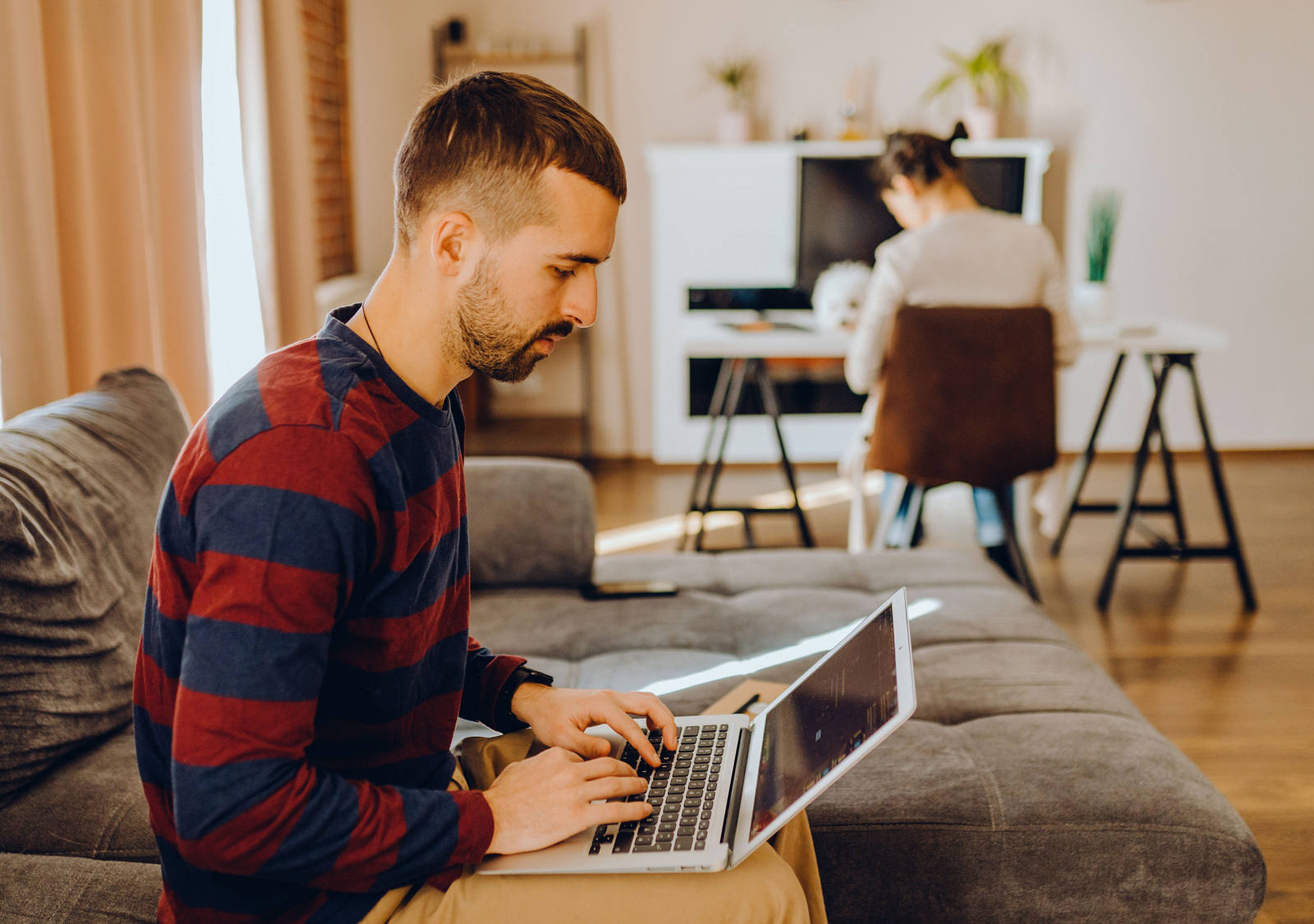 Man works on the laptop and sits on the sofa.