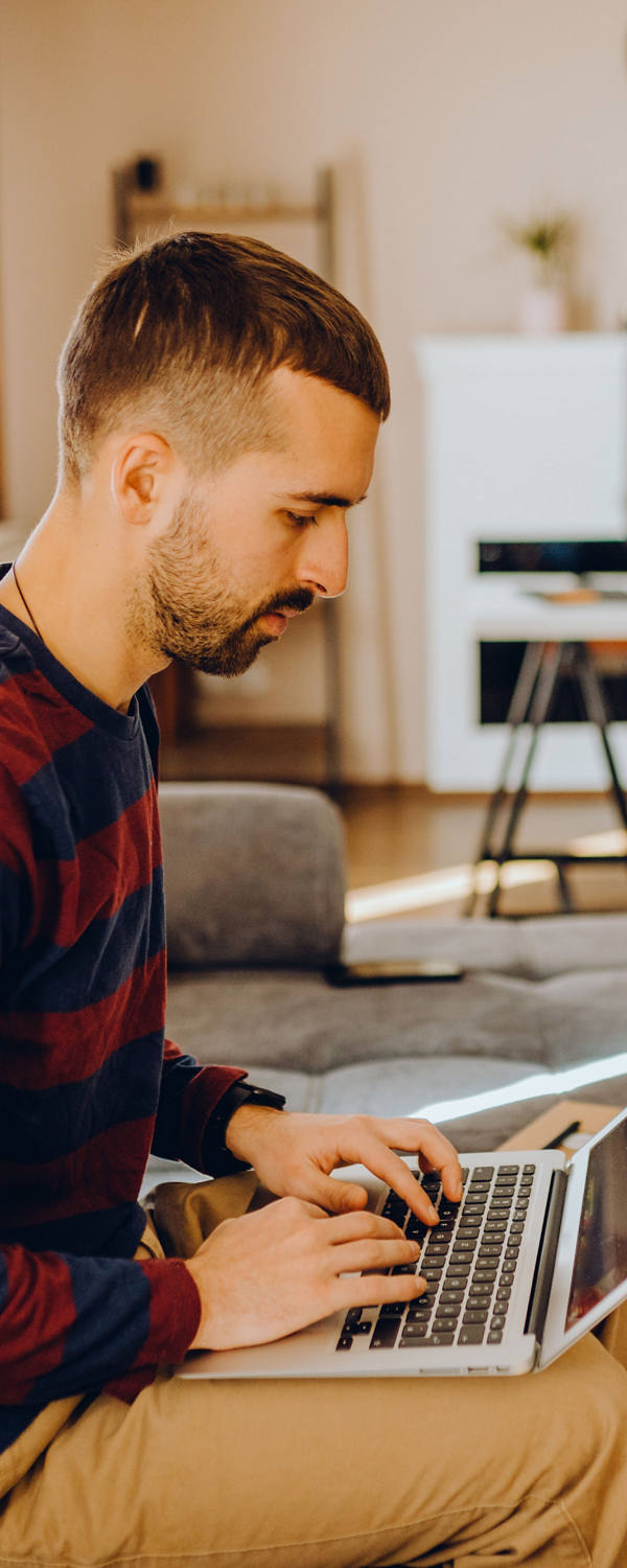 L’uomo lavora al portatile e si siede sul divano.